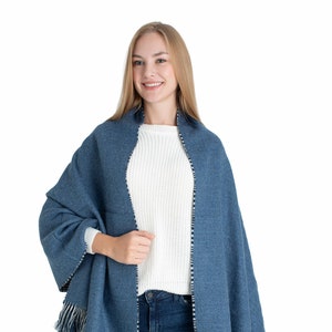 Peut inclure: Une écharpe bleue à franges avec une bordure blanche et noire. L'écharpe est drapé autour des épaules d'une personne.