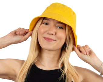 May include: A woman wearing a yellow bucket hat and a black tank top. She is smiling and looking at the camera.