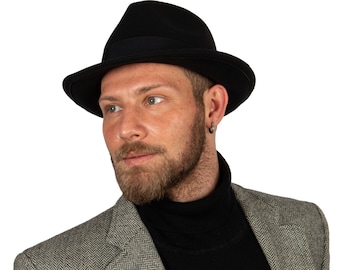 May include: A man wearing a black fedora hat, a black turtleneck sweater, and a grey herringbone blazer.