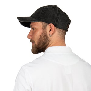 Könnte beinhalten: Eine schwarze, gewaschene Baseballkappe aus Baumwolle mit einem gebogenen Schirm. Die Kappe wird von einer Person mit Bart und einem weißen Poloshirt getragen.