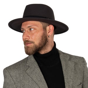 Könnte beinhalten: Ein Mann trägt einen schwarzen Fedora-Hut mit einem schwarzen Rollkragenpullover und einem grauen Fischgrätenblazer.
