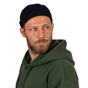 May include: A man wearing a dark green hooded sweatshirt and a black beanie.