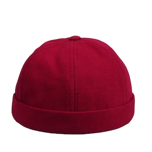 Puede incluir: Gorra tipo skull cap de color burdeos con borde doblado. El gorro está hecho de tela texturizada y tiene una corona redondeada. Un sombrero clásico para atuendos informales. El gorro es de color rojo oscuro.