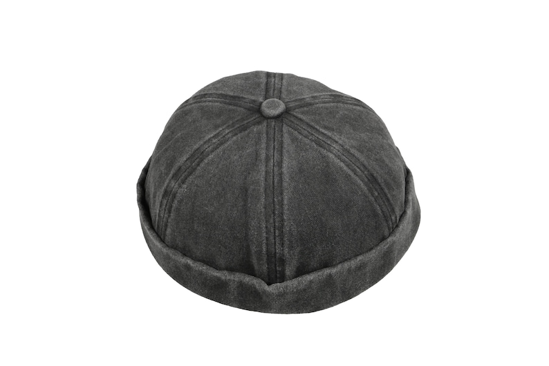 May include: A dark gray, unisex docker hat with a rolled brim. The hat features a button on top and stitched detailing across the crown. This casual hat is suitable for various outfits and weather conditions.