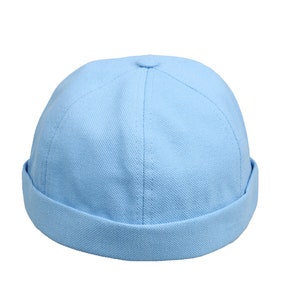 Peut inclure: Un chapeau docker en coton bleu clair. Le chapeau a une couronne arrondie et un bord replié. Le chapeau est fait d'un tissu texturé et est de couleur bleu clair uni. Le chapeau est de style décontracté.