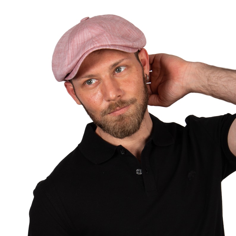 May include: A man wearing a pink linen newsboy cap and a black polo shirt.