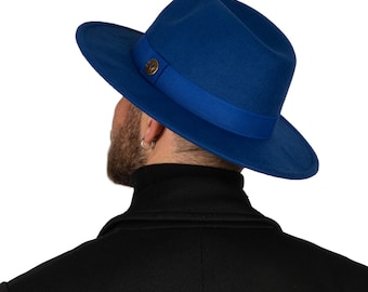 May include: A blue fedora hat with a matching blue band and a gold button. The hat is worn by a person with a black turtleneck shirt.