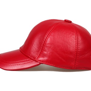 Op de afbeelding: Een felrode baseballcap van leer. De cap heeft een gebogen klep en een knoop aan de bovenkant. De naden zijn zichtbaar. Een klassiek accessoire.