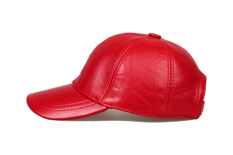 Op de afbeelding: Een felrode baseballcap van leer. De cap heeft een gebogen klep en een knoop aan de bovenkant. De naden zijn zichtbaar. Een klassiek accessoire.
