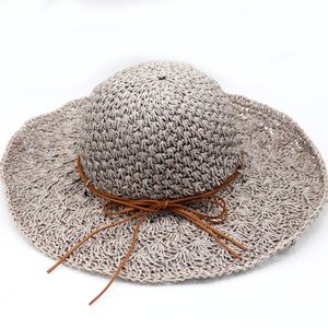 May include: A light gray crocheted sun hat with a brown leather ribbon tied in a bow.