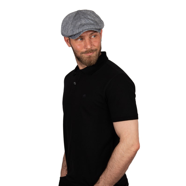 May include: A man wearing a gray newsboy cap and a black polo shirt. He is looking over his shoulder.