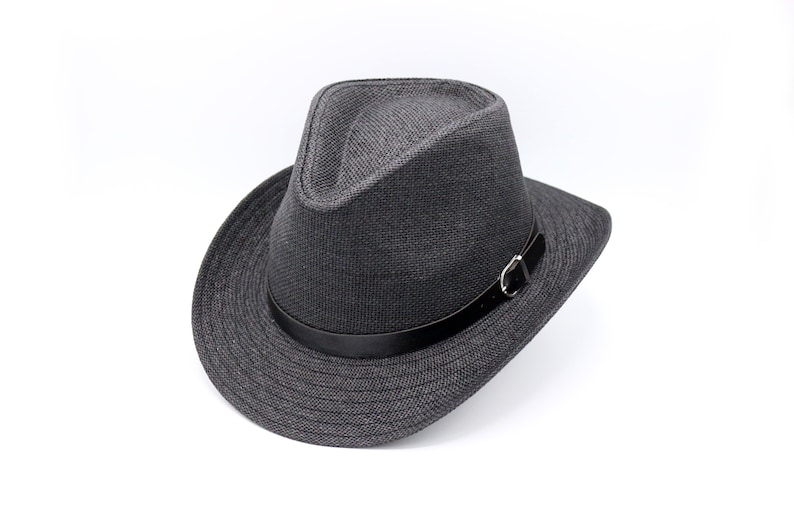 K&ouml;nnte beinhalten: Ein grauer Fedora-Hut mit einem schwarzen Lederband und einer silbernen Schnalle. Der Hut hat eine breite Krempe und eine leicht eingedellte Krone.