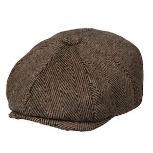 Op de afbeelding: Een bruine newsboy-pet met visgraatpatroon. De pet heeft een ronde kroon en een korte, stijve klep. De stof heeft een getextureerde uitstraling met bruine en beige draden, wat een klassieke, vintage look creëert. Deze hoed is geschikt voor diverse gelegenheden.