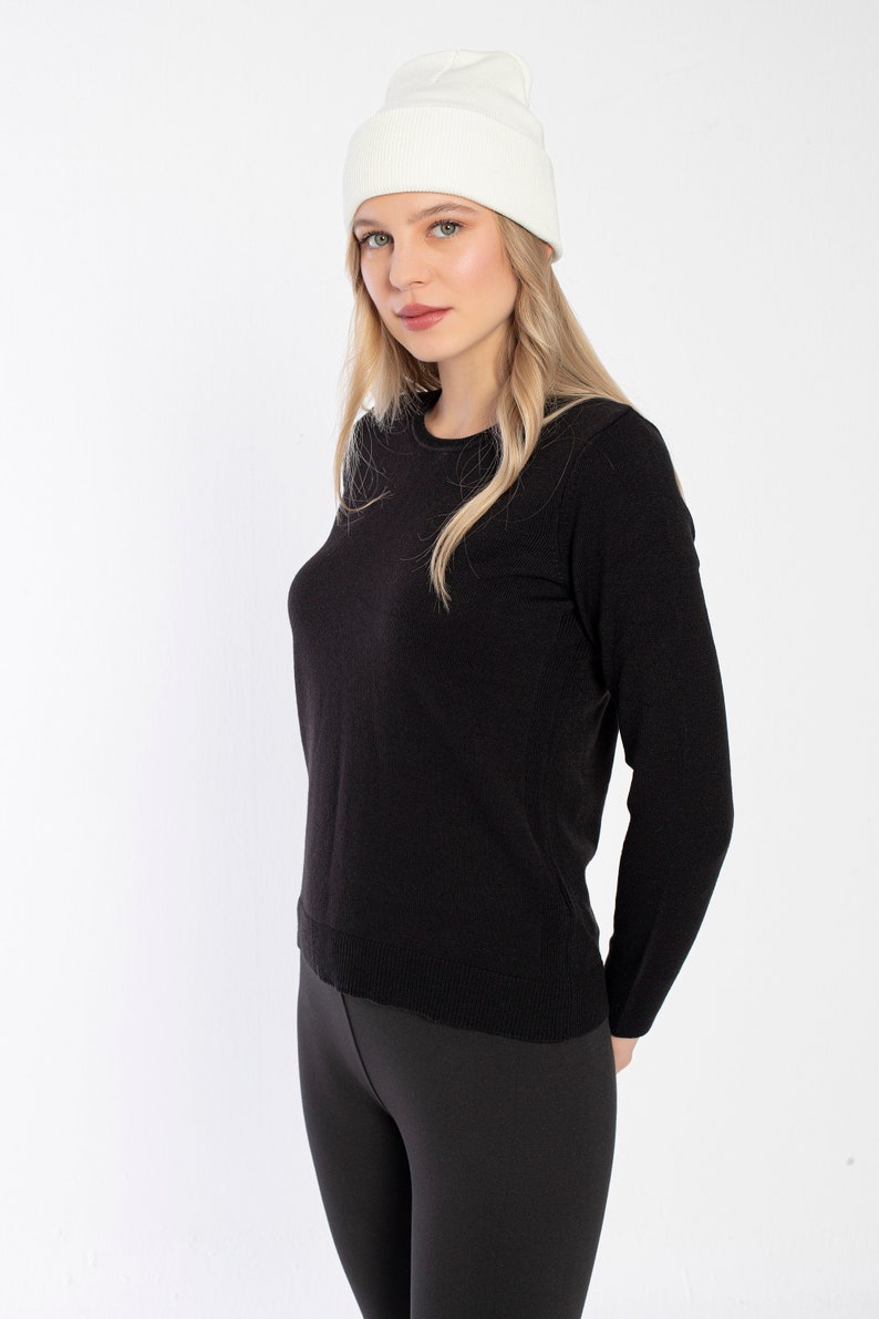 K&ouml;nnte beinhalten: Eine Frau tr&auml;gt einen schwarzen Langarm-Pullover und schwarze Leggings mit einer wei&szlig;en M&uuml;tze.