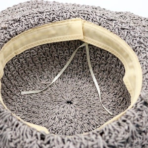 May include: The inside of a gray crocheted hat with a beige fabric band around the edge. A white ribbon is tied inside the hat.