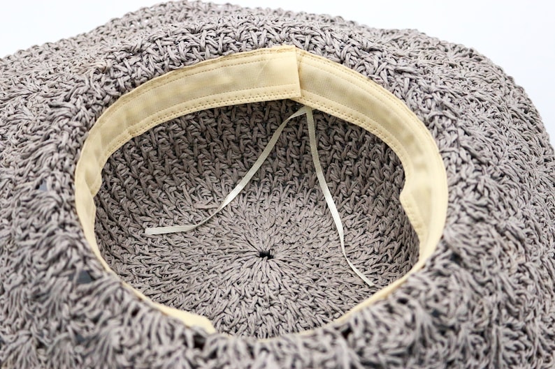 May include: The inside of a gray crocheted hat with a beige fabric band around the edge. A white ribbon is tied inside the hat.