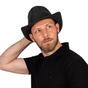 K&ouml;nnte beinhalten: Ein Mann tr&auml;gt ein schwarzes Poloshirt und einen schwarzen Fedora-Hut. Er schaut nach rechts und hat einen Bart.