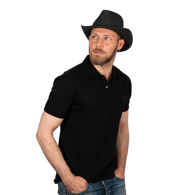 K&ouml;nnte beinhalten: Ein Mann tr&auml;gt ein schwarzes Poloshirt und einen schwarzen Cowboyhut. Er schaut nach rechts aus dem Bild.