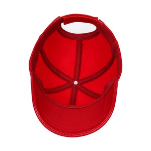 Op de afbeelding: Een felrode baseballcap, van binnenuit bekeken, met de interne structuur. De cap heeft een gebogen klep en een verstelbare band. De binnenkant heeft een donkerrode voering en een centrale knop.
