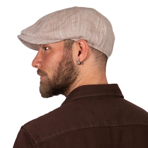 Puede incluir: Una gorra de newsboy de lino beige con una visera ligeramente curvada. La gorra está hecha de un tejido suave y ligero y tiene un aspecto informal y relajado.