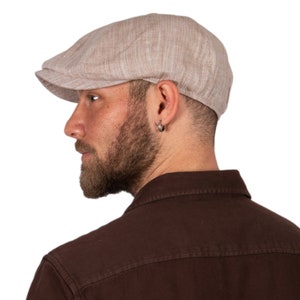 May include: A man wearing a light brown linen newsboy cap with a brown button-down shirt.