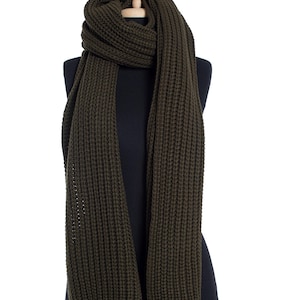 Puede incluir: Una bufanda de punto verde oscuro en un maniquí negro. La bufanda es larga y ancha, con una textura acanalada.