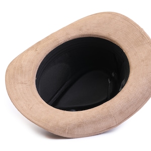 May include: A brown suede fedora hat with a black mesh lining. The hat is turned inside out, showing the lining.