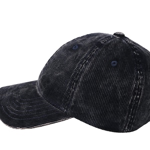 Puede incluir: Una gorra de béisbol de pana azul marino oscuro con una textura desgastada y lavada. La gorra presenta una visera curva, una construcción de seis paneles con ojales cosidos, un botón superior cubierto de tela y un cierre de correa metálica ajustable.