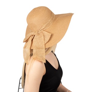 May include: A wide-brimmed straw hat with a large bow tied at the back. The hat is a light brown colour and has a slightly textured finish.