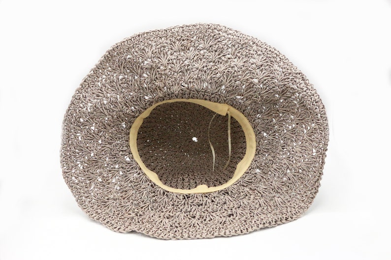 May include: A light brown crocheted sun hat with a cream colored lining. The hat is made of a woven material and has a wide brim.