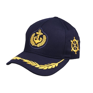 May include: A navy blue baseball cap with a gold anchor and laurel wreath embroidered on the front. The cap also has a gold steering wheel embroidered on the side and a gold laurel wreath embroidered on the brim.