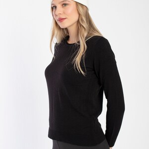 K&ouml;nnte beinhalten: Eine Frau tr&auml;gt einen schwarzen Langarm-Pullover und schwarze Leggings mit einer wei&szlig;en M&uuml;tze.