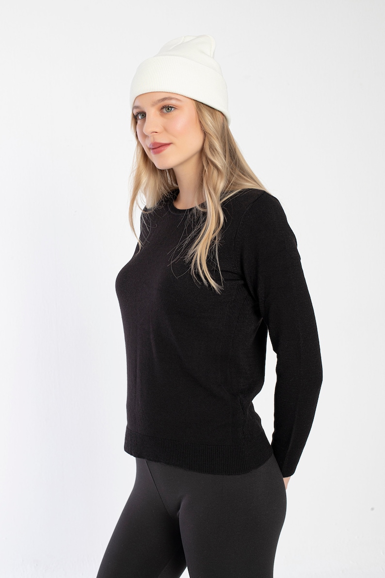 K&ouml;nnte beinhalten: Eine Frau tr&auml;gt einen schwarzen Langarm-Pullover und schwarze Leggings mit einer wei&szlig;en M&uuml;tze.