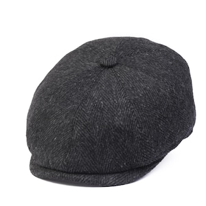 Op de afbeelding: Een zwarte newsboy-pet met een herringbone-patroon.