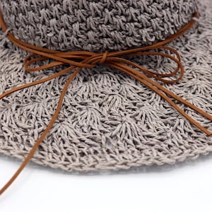 May include: A gray crocheted sun hat with a brown leather tie. The hat has a wide brim and is made of a lightweight material.