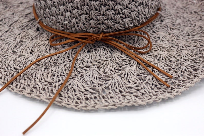 May include: A gray crocheted sun hat with a brown leather tie. The hat has a wide brim and is made of a lightweight material.