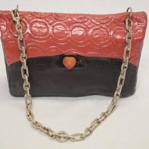 May include: A red and black ceramic purse with a heart-shaped detail and a silver chain strap.