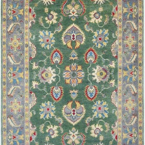 Peut inclure: Un tapis rectangulaire présentant un champ central vert profond orné d'un motif floral symétrique dans des tons de rouge, bleu, jaune et crème. Le tapis est encadré par une large bordure bleu sourd avec des motifs floraux répétés.