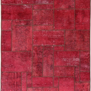 Op de afbeelding: Een rood patchwork tapijt met een geometrisch patroon. Het tapijt is gemaakt van verschillende stukken stof die aan elkaar zijn genaaid.