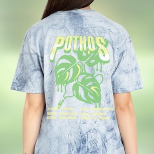 Puede incluir: Una camiseta azul claro tie-dye con un gráfico verde y amarillo de una planta con la palabra "POTHOS" impresa.