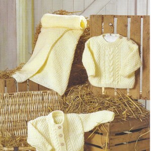 May include: A selection of knitted baby garments in pale yellow. The image shows a blanket, a sweater with cable knit design, and a button-up cardigan. The text "James C. Brett" and "JB783 Difficult Knit" are visible.
