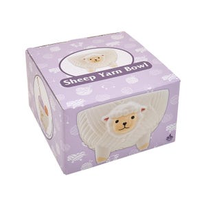 May include: A lavender box featuring a white sheep yarn bowl. The box has a repeating pattern of white yarn balls and sheep. The yarn bowl is white and shaped like a sheep. The text "Sheep Yarn Bowl" is printed on the box.