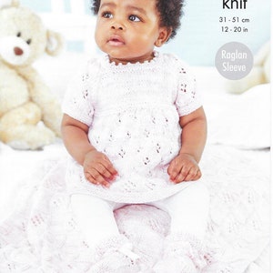 May include: A baby in a light pink knitted dress, leggings, and booties. The dress features a scalloped neckline and short sleeves. The text "5856 double knit" and "Raglan Sleeve" are visible. The baby is sitting on a pink blanket, with measurements 31-51 cm.