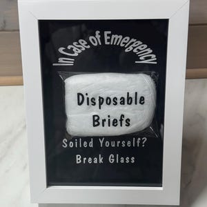 Könnte beinhalten: Ein weißer Rahmen mit dem Text "In Case of Emergency" über einer Packung Einweg-Slips. Darunter steht der Text "Soiled Yourself? Break Glass."