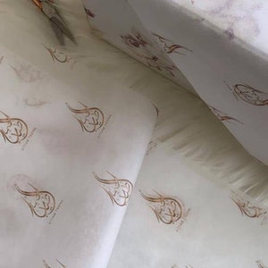 May include: White tissue paper with a repeating pattern of a gold calligraphy design that says "Atwar Teema".