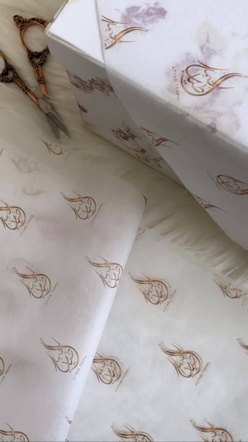 May include: White tissue paper with a repeating pattern of a gold calligraphy design that says "Atwar Teema".