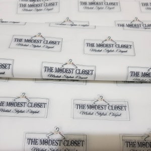 May include: White wrapping paper with a repeating pattern of a black and white logo that says "The Modest Closet" with a hanger and floral design. The text below the logo says "Modest. Stylish. Elegant."