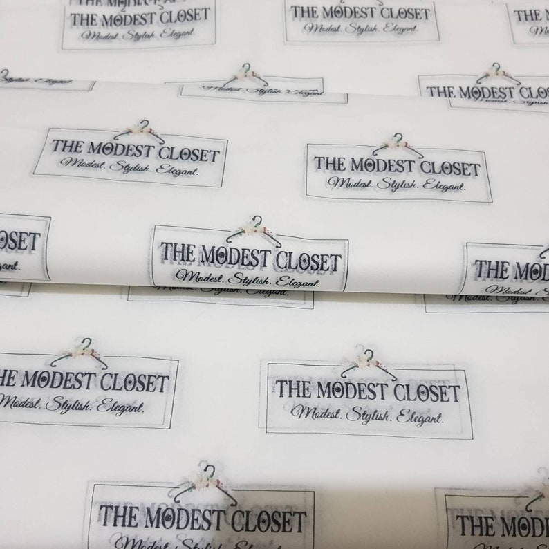 May include: White wrapping paper with a repeating pattern of a black and white logo that says "The Modest Closet" with a hanger and floral design. The text below the logo says "Modest. Stylish. Elegant."