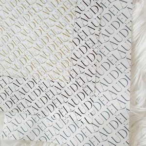 May include: Three sheets of wrapping paper with a repeating pattern of the word "AUDELA" in black, gold, and gray.
