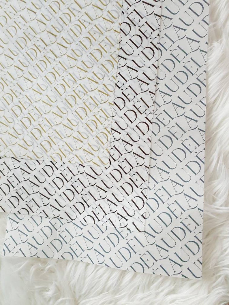 May include: Three sheets of wrapping paper with a repeating pattern of the word "AUDELA" in black, gold, and gray.